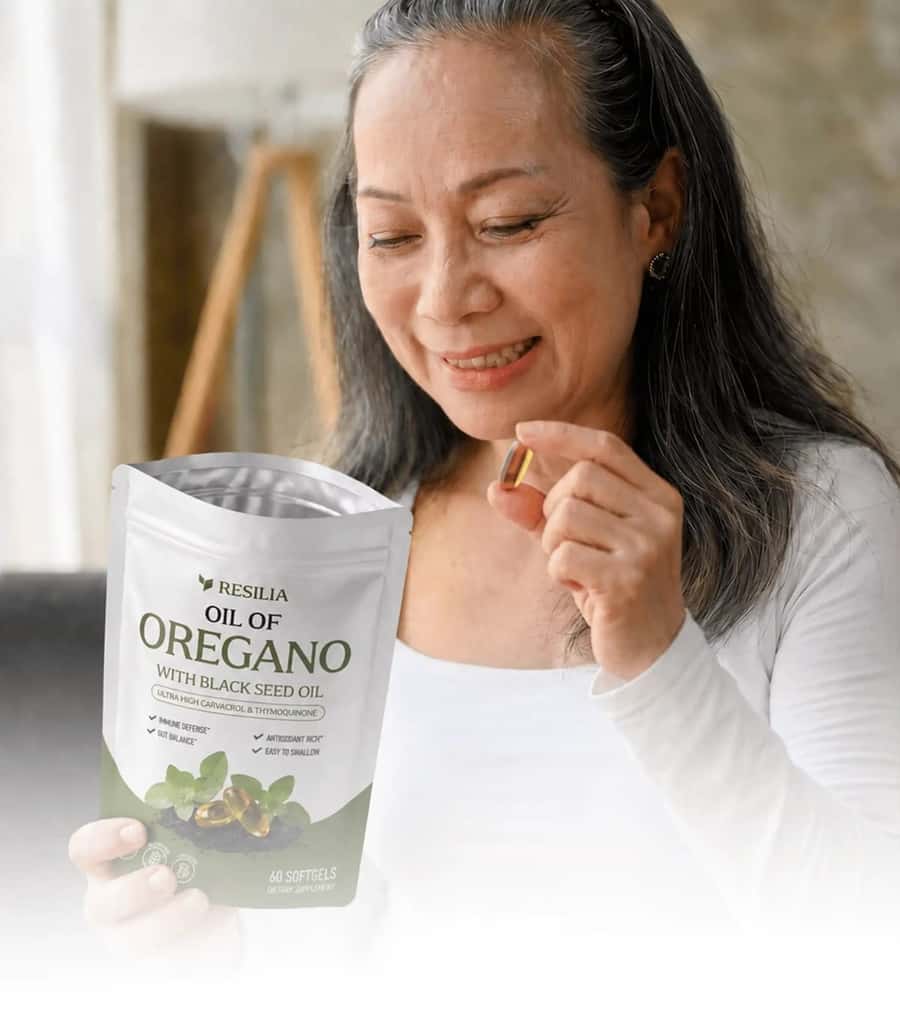 A woman smiling as she takes a Resilia softgel at home